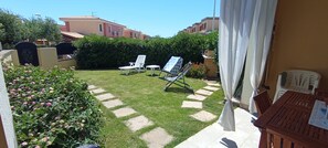 A backyard with a lawn, two lounge chairs, a small table, and a wooden bench. - Casa Luca in the Borghi of Villasimius  (Sardegna)