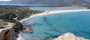 A coastal landscape with a beach, clear blue waters, and mountainous terrain in the background. - Casa Luca in the Borghi of Villasimius  (Sardegna)