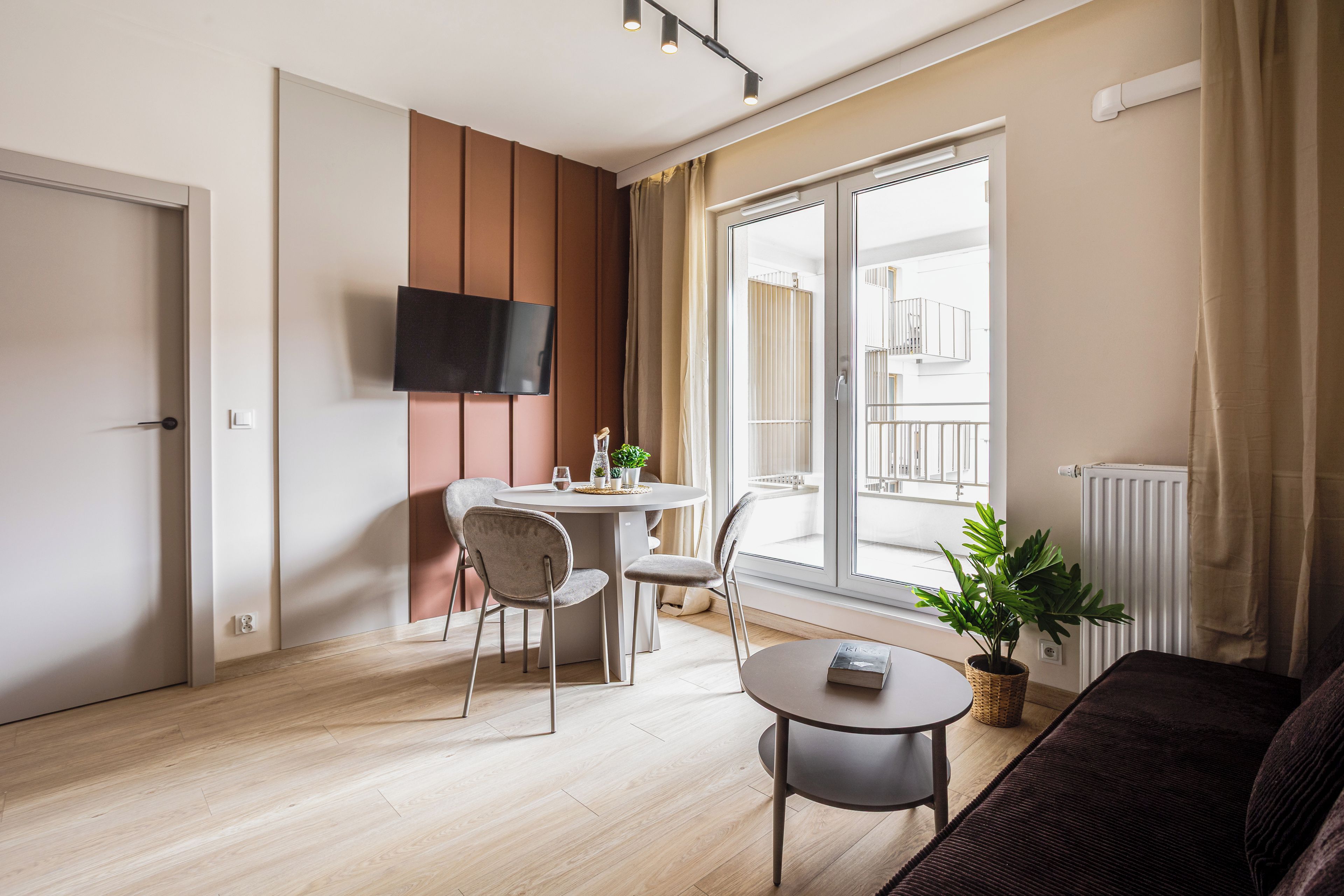 Un salón moderno con un televisor de pantalla plana montado en la pared, una mesa redonda con sillas, una planta en maceta y un sofá.
