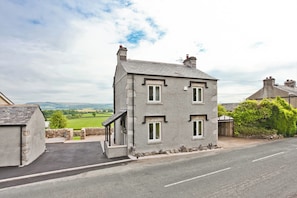 A two-story stone house with a paved driveway and a view of the countryside. - Hillberry Cottage (Carnforth)