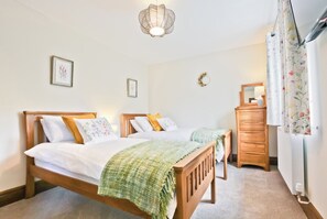 A bedroom with two wooden beds, a dresser, a mirror, and a hanging light fixture. - Hillberry Cottage (Carnforth)