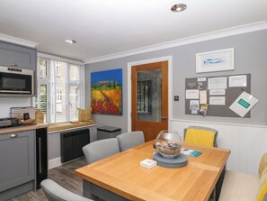 A modern kitchen with a built-in microwave, a dining area with a wooden table, and a painting on the wall. - 12 Courtyard Cottage at Sheplegh Court (Totnes)