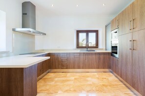 A modern kitchen with wooden cabinets, a stainless steel range hood, a window, and a built-in oven. - Modern Rustic Country Villa with Pool (Lloseta)