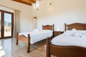 A hotel room with two wooden beds, a nightstand with a lamp, and a view through a large window. - Modern Rustic Country Villa with Pool (Lloseta)