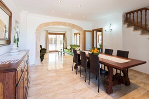 A dining area with a marble floor, a wooden dining table, and chairs. There is a green sofa in the background. - Modern Rustic Country Villa with Pool (Lloseta)