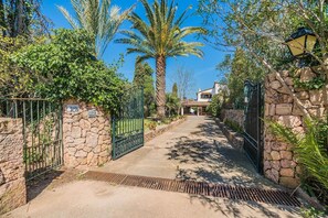 A pathway leading to a house with stone walls and metal gates, surrounded by greenery and palm trees. - Charming Chalet for 8 in Pollensa (Pollensa / Pollença)