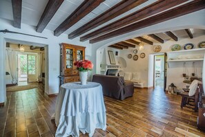A spacious room with a wooden floor, a round table with a vase of flowers, a sofa, and a cabinet with glass doors. - Charming Chalet for 8 in Pollensa (Pollensa / Pollença)
