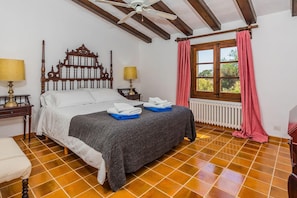A bedroom with a wooden bed, two bedside lamps, a window with curtains, and a radiator. - Charming Chalet for 8 in Pollensa (Pollensa / Pollença)
