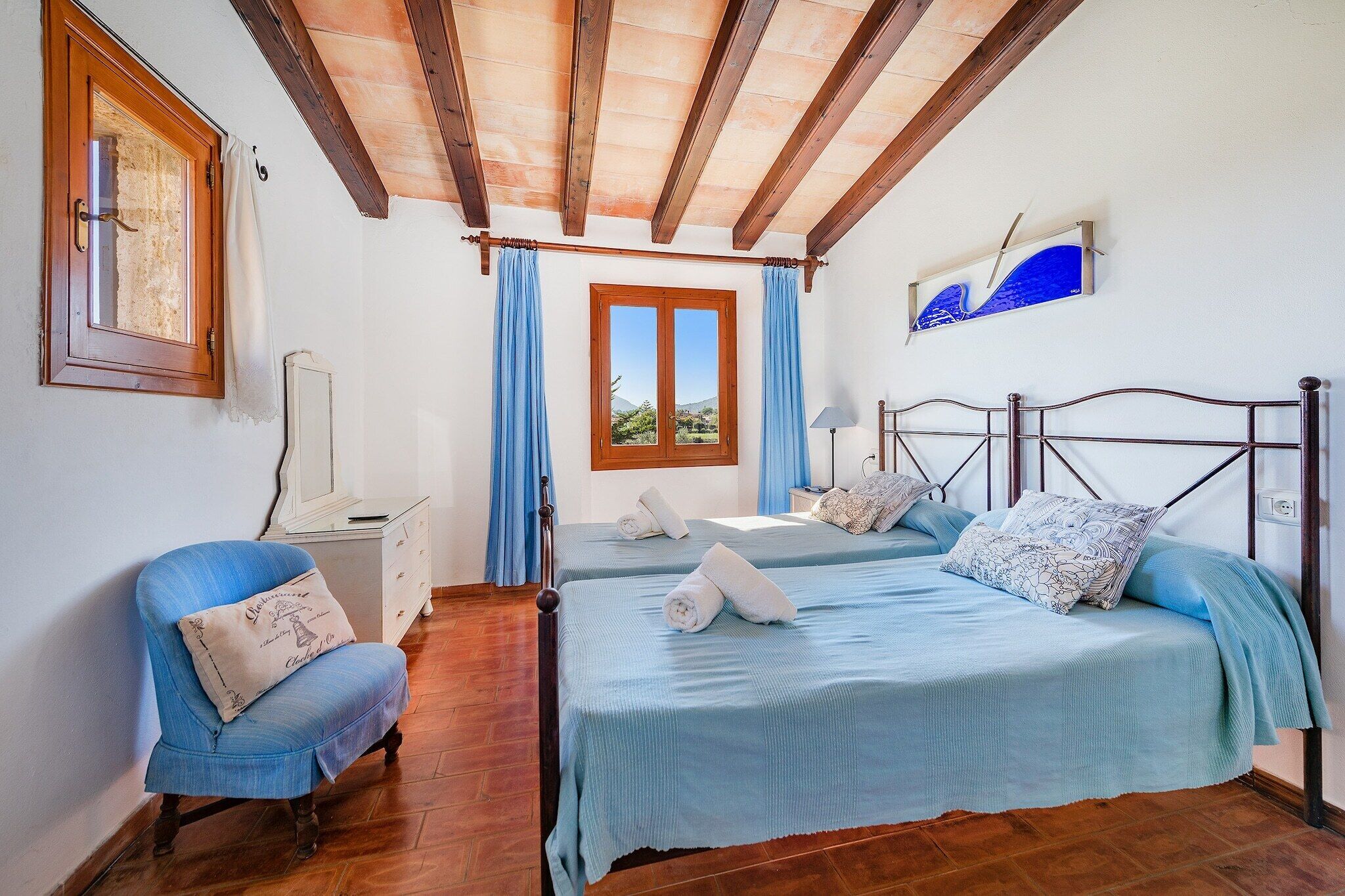 Quarto com duas camas, uma cadeira, escrivaninha e janela com cortinas.