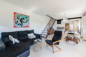 A modern living room with a black sofa, a blue armchair, and a coffee table. There is a staircase leading to a kitchen area. - Pollensa Country Villa for 6 (Pollensa / Pollença)