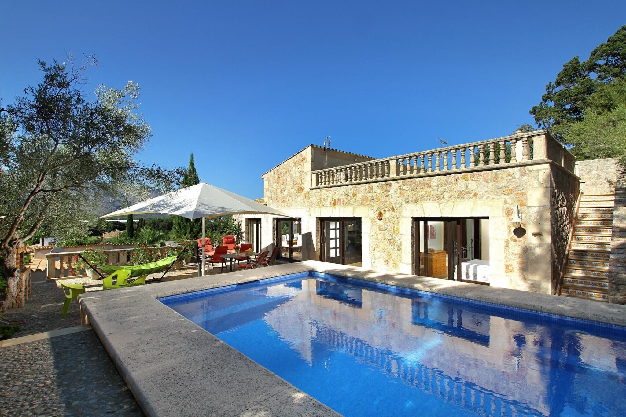 A swimming pool with a stone building adjacent to it, featuring a balcony and outdoor seating area.