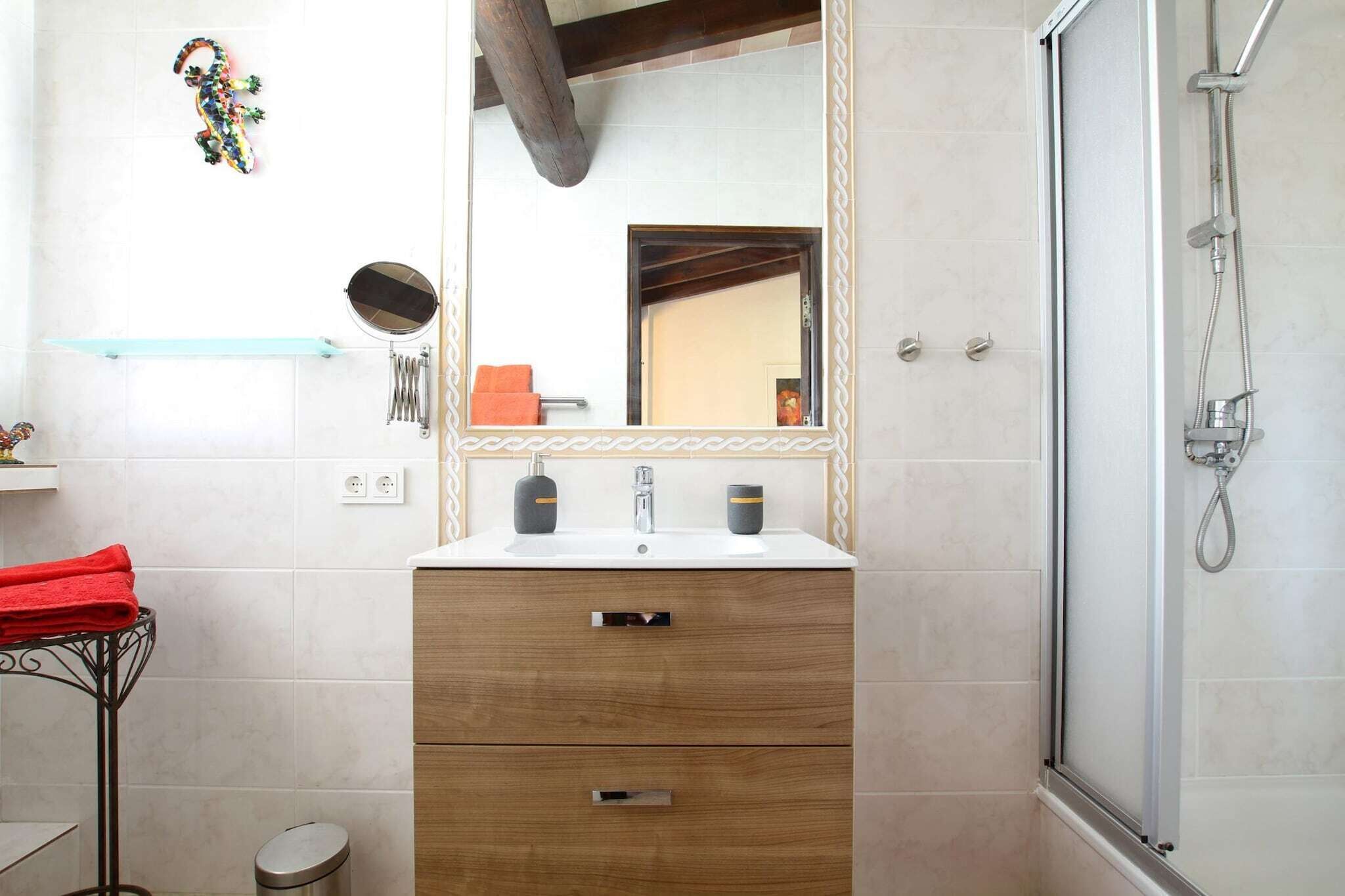A bathroom with a wooden vanity, a mirror, a shower, and a small shelf with a towel.