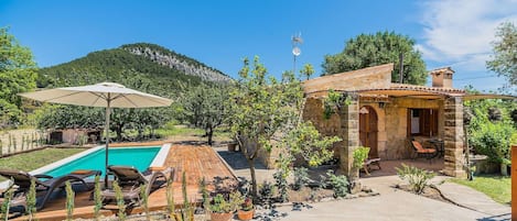 Ein Poolbereich mit Liegestühlen, ein kleines Gebäude mit Terrasse und eine gebirgige Kulisse.