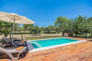 A rectangular swimming pool with a wooden deck surrounding it, a lounge chair, and a large umbrella. - Romantic Country Hideaway in Pollensa (Pollensa / Pollença)