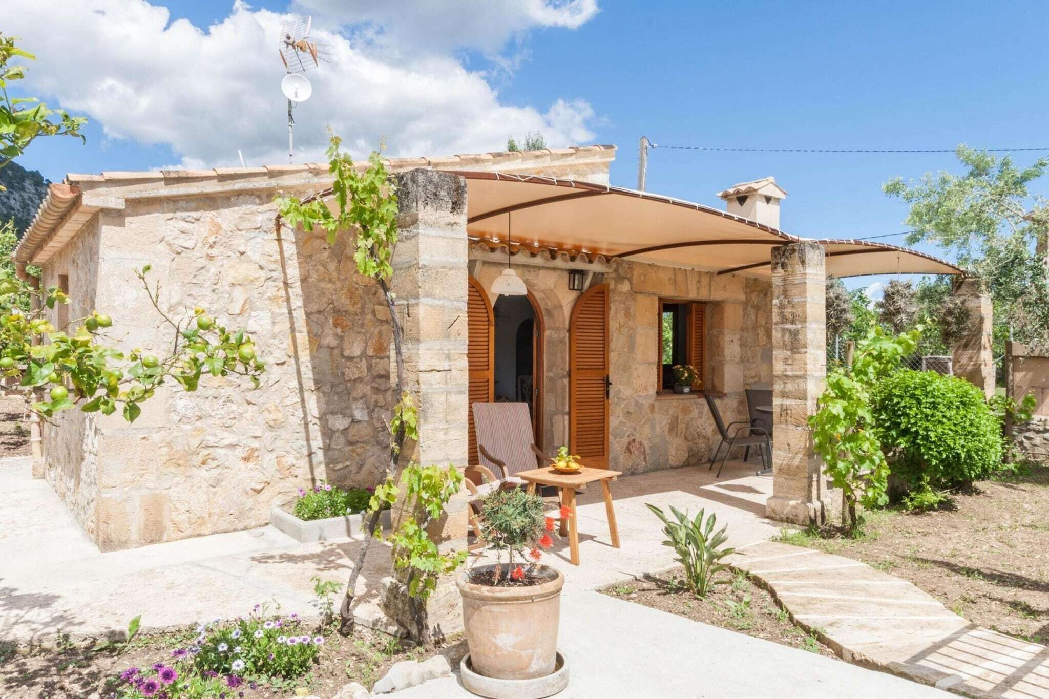 A stone building with a covered patio, a table with chairs, and potted plants.