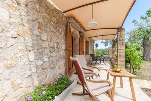 A stone wall with a covered patio area featuring a table and chairs. - Romantic Country Hideaway in Pollensa (Pollensa / Pollença)