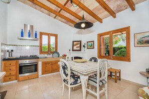 A kitchen with wooden cabinets, a gas stove, and a dining area with a table and chairs. - Romantic Country Hideaway in Pollensa (Pollensa / Pollença)