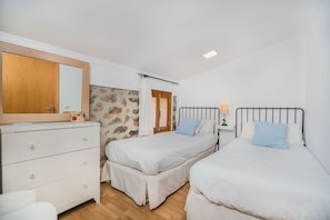 A bedroom with two beds, a dresser, a mirror, and a stone wall. - CASETA DE LLOSETA Ref VP22 1 (Lloseta)