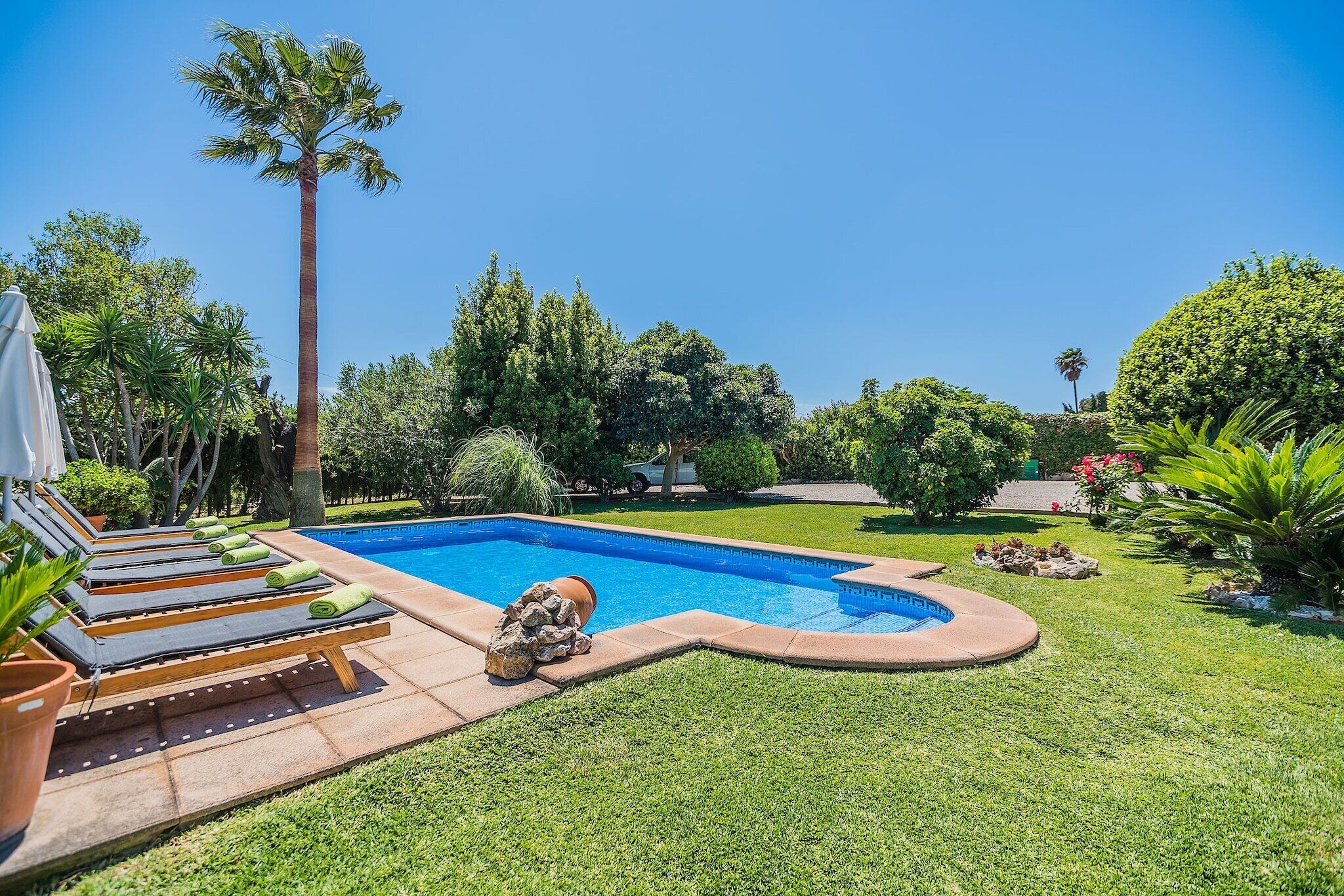 A swimming pool with a surrounding grassy area and lounge chairs.