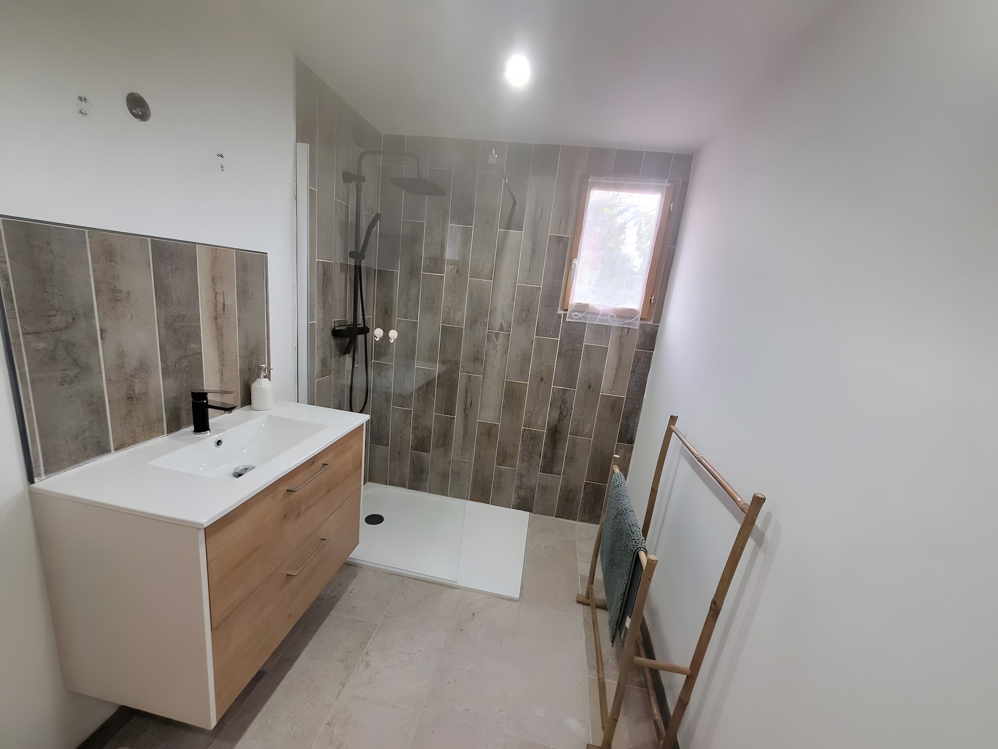Een moderne badkamer met een witte wastafel, een douche met glazen deur en een klein raam.