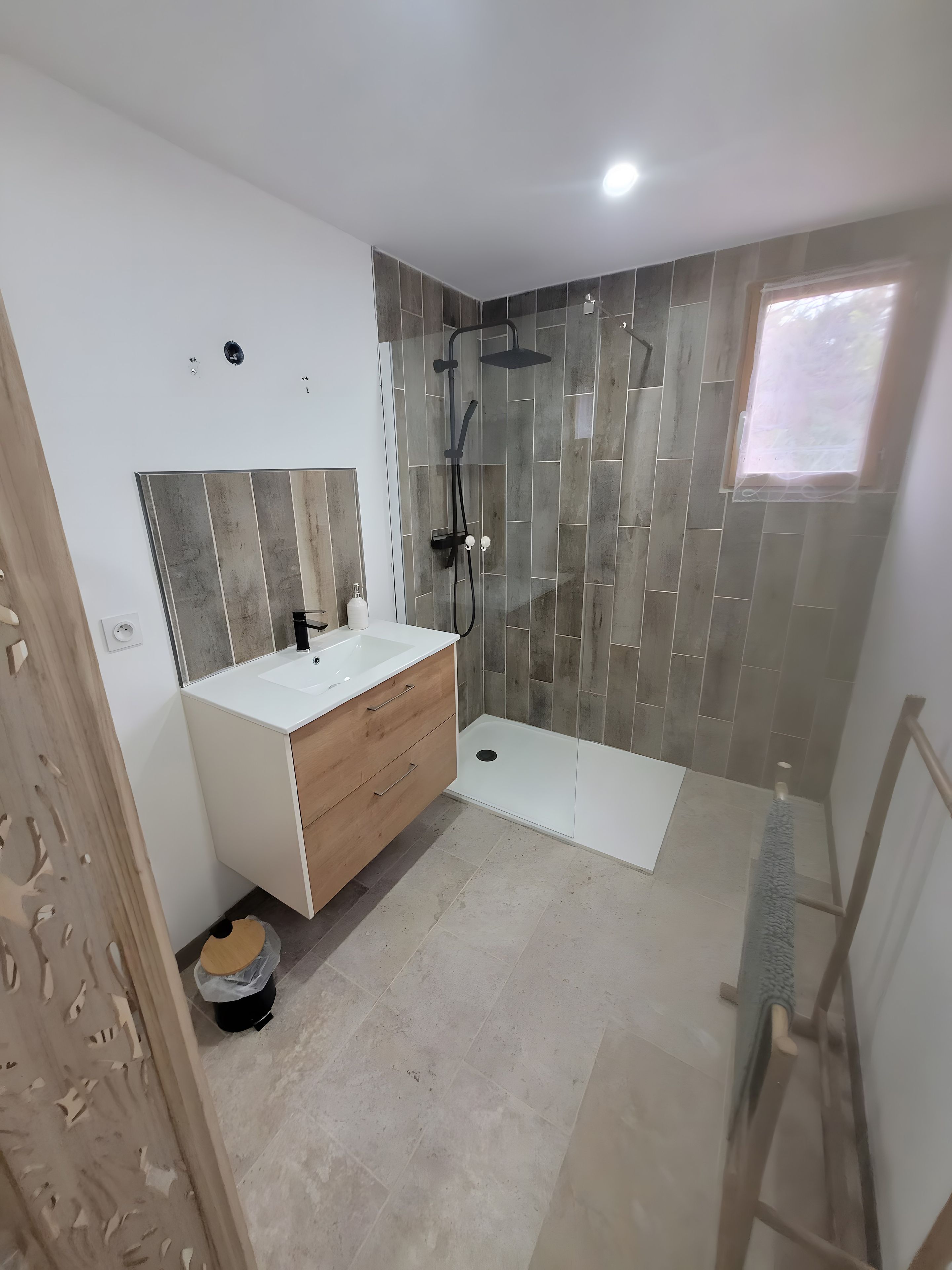 Un baño moderno con un lavabo blanco, tocador de madera y zona de ducha con puerta de vidrio.