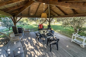 An outdoor deck with wooden flooring, a table with chairs, and a hanging light fixture. - Gîte M with Shared Pools, Wi-Fi & Air Conditioning in Codognan (Codognan)