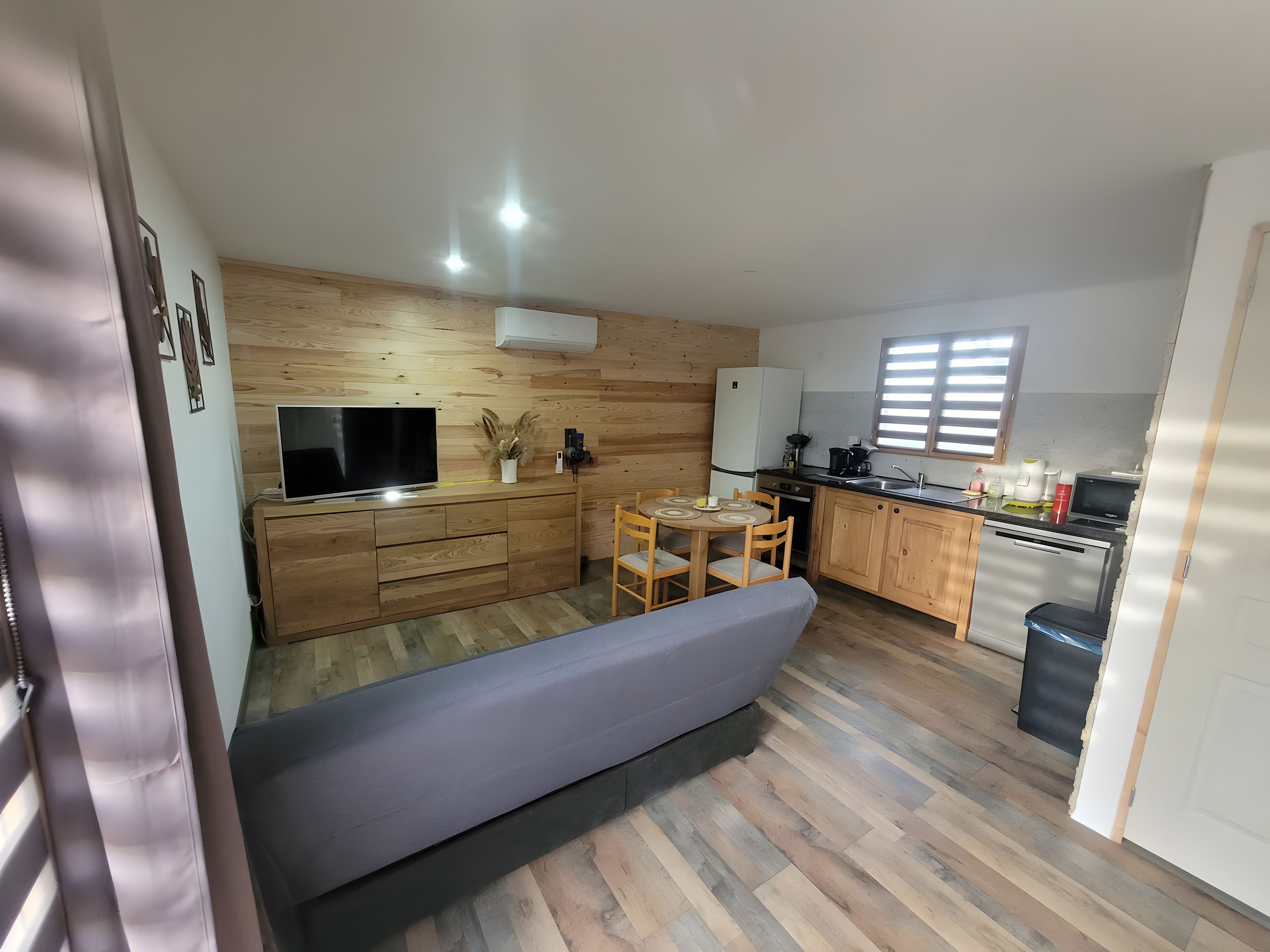 A compact living space with a sofa, a TV, a dining table, and a kitchenette.