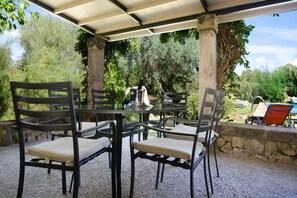 An outdoor patio with a table and chairs, a stone wall, and a pool in the background. - Traditional Villa with Pool in Pollensa (Pollensa / Pollença)