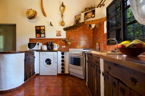 A kitchen with a washing machine, oven, and a bowl of fruit on the counter. - Traditional Villa with Pool in Pollensa (Pollensa / Pollença)