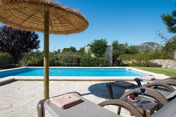 A swimming pool with lounge chairs and an umbrella, surrounded by greenery and a stone wall. - Stone Majorcan Villa with Gardens (Pollensa / Pollença)