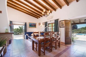 A dining area with wooden furniture, a chandelier, and a view of the outdoors. - Stone Majorcan Villa with Gardens (Pollensa / Pollença)