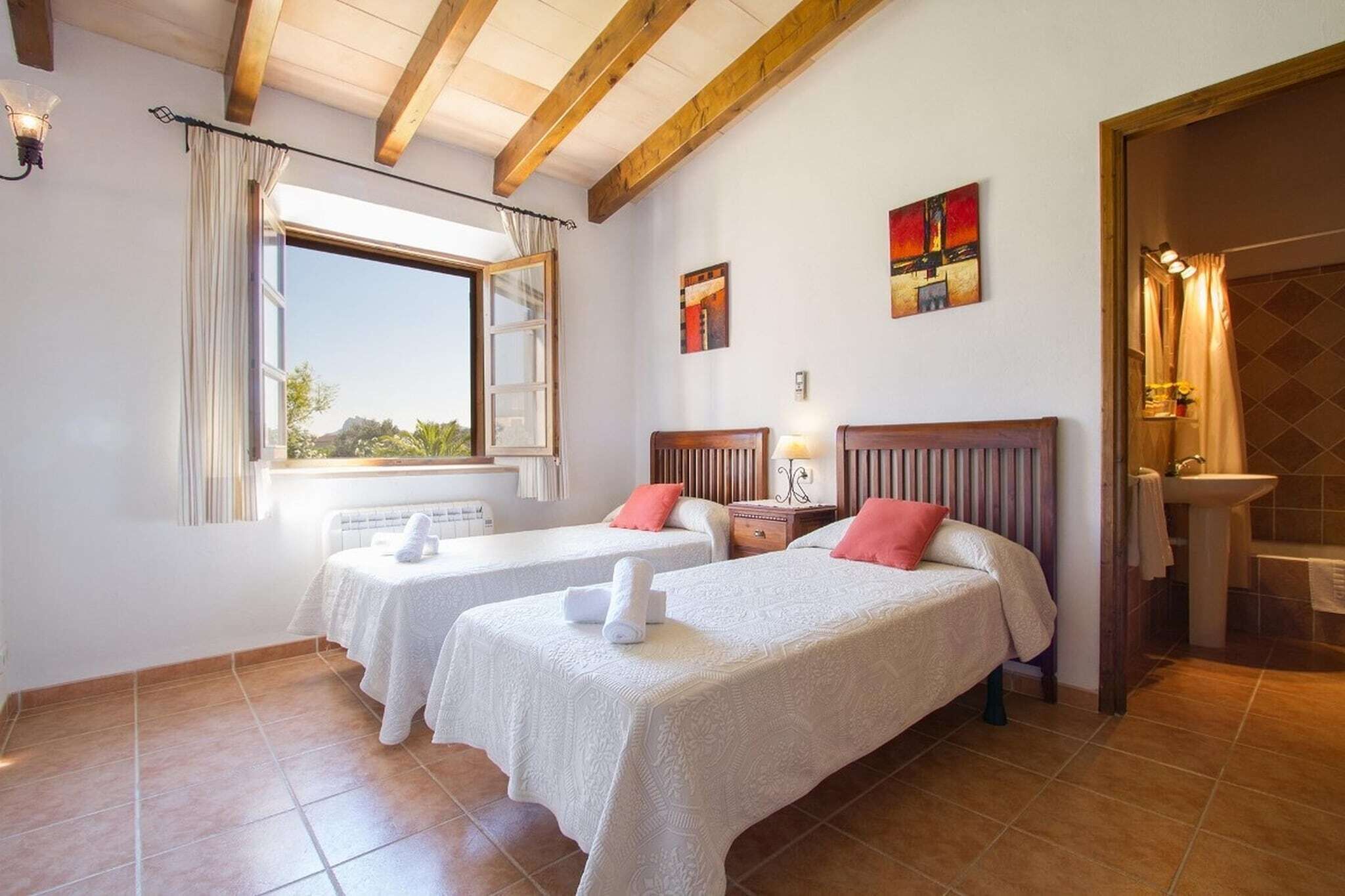 Une chambre d’hôtel avec deux lits, une fenêtre, des œuvres d’art accrochées aux murs et une salle de bain visible par une porte ouverte.