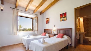 Quarto de hotel com duas camas, uma janela, obras de arte nas paredes e um banheiro visível através de uma porta aberta.