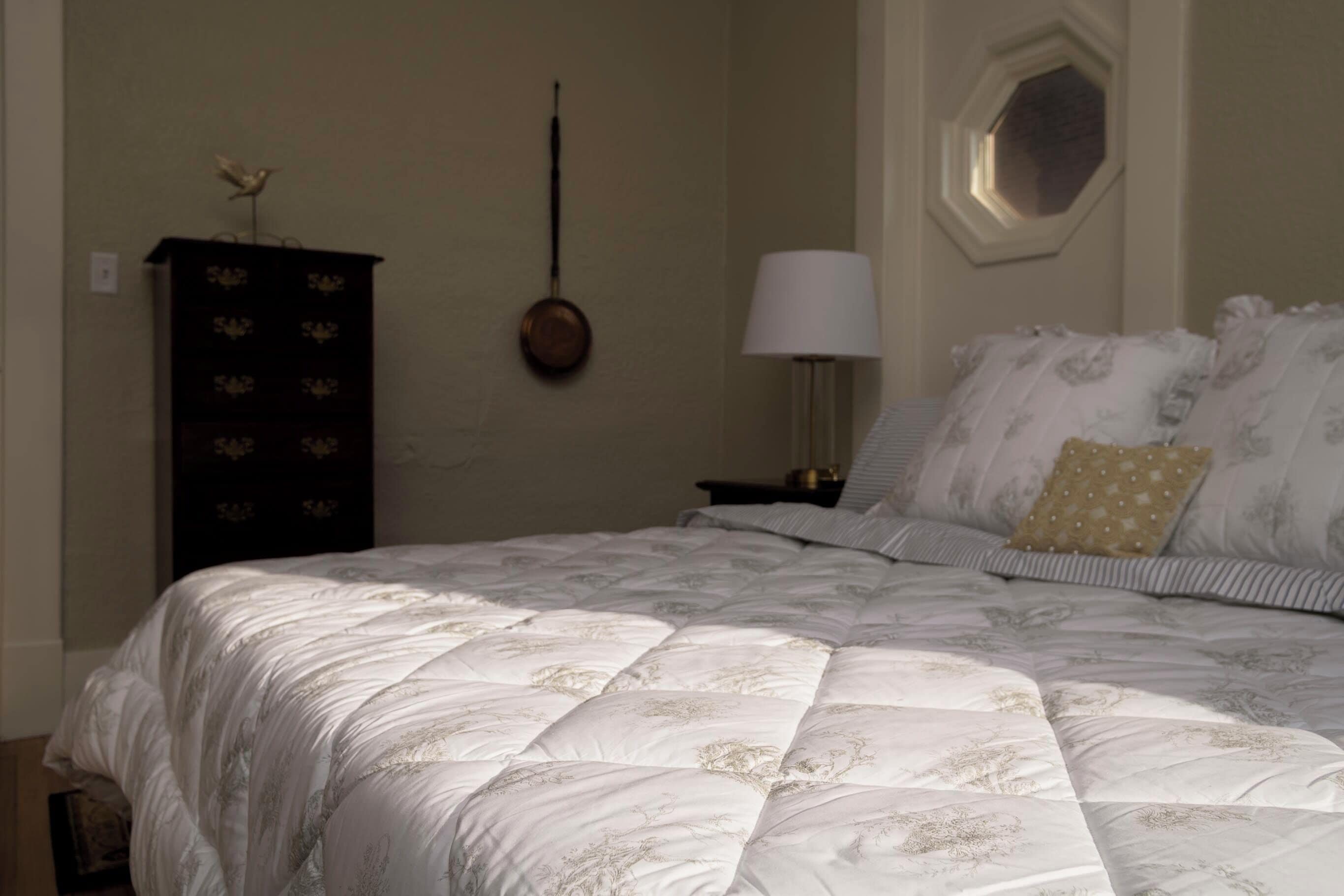 A bedroom with a large bed, a dresser, a wall-mounted lamp, and a window.