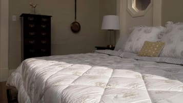 A bedroom with a large bed, a dresser, a wall-mounted lamp, and a window.