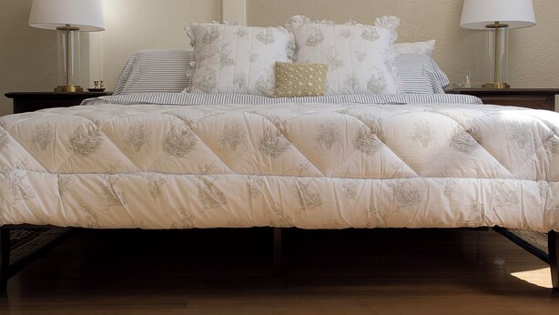 Un dormitorio con una cama grande, dos mesitas de noche con lámparas, un ventanal con diseño geométrico y una pared con textura.