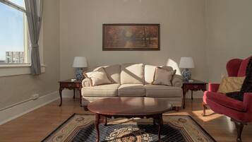 A living room with a sofa, two side tables with lamps, a red armchair, a coffee table, and a painting on the wall.