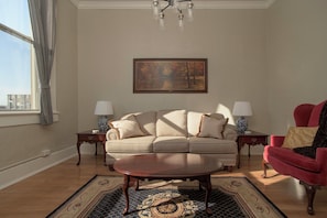 A living room with a sofa, two side tables with lamps, a red armchair, a coffee table, and a painting on the wall.