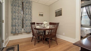 Un comedor con mesa y sillas de madera, una cortina floral y dos cuadros en la pared.
