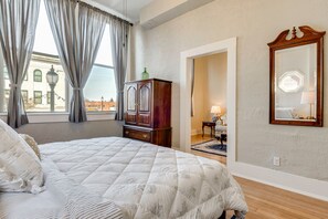 A hotel room with a large bed, a wooden cabinet, a mirror, and a view of the city through the window. - Historic Downtown Stay on the Square (Lebanon)