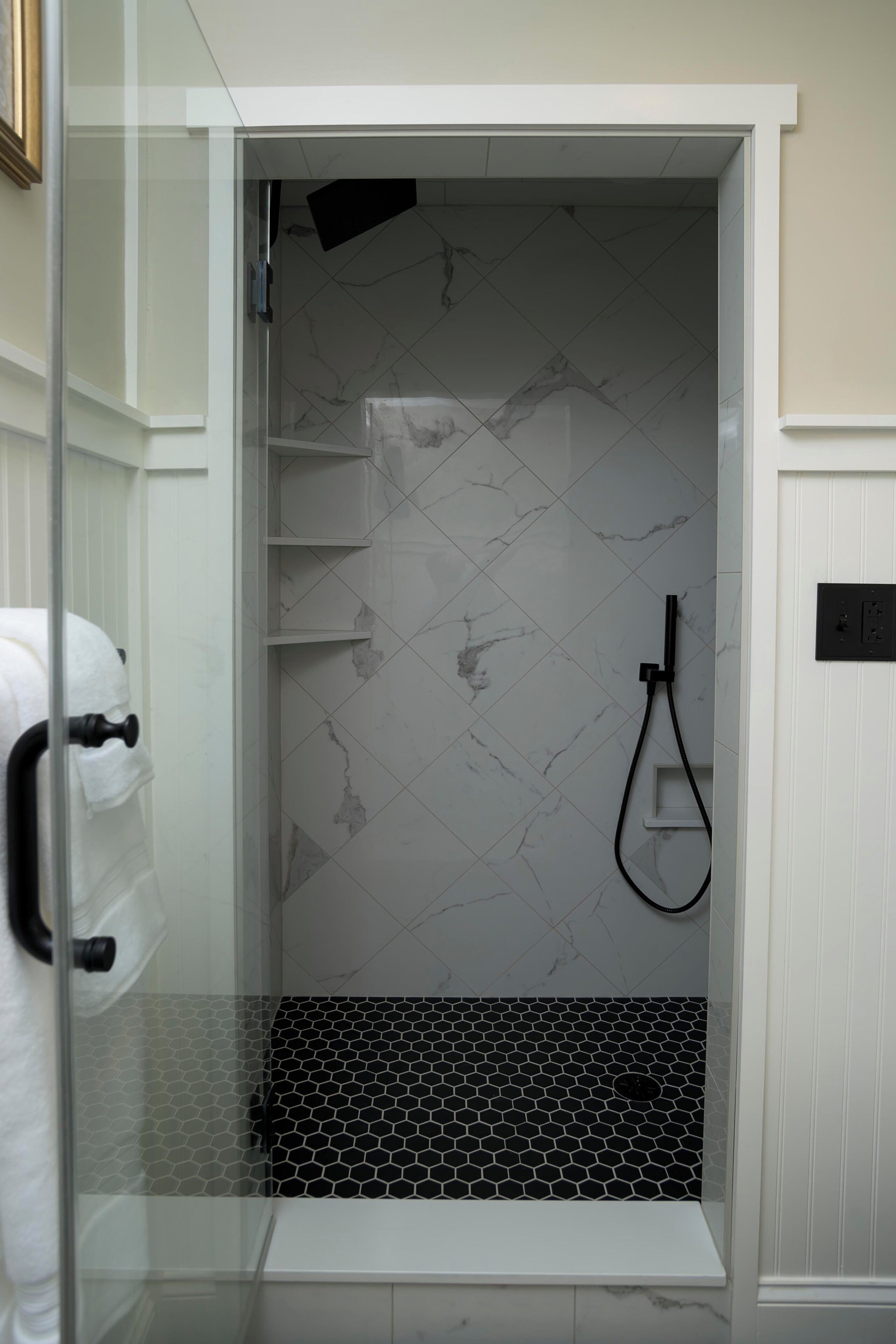 A modern bathroom with a glass shower enclosure, marble tiles, and a black and white hexagonal tile pattern on the floor.