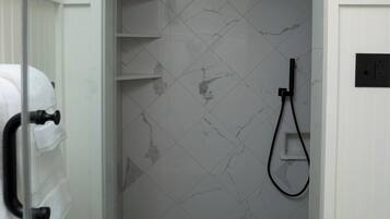 A modern bathroom with a glass shower enclosure, marble tiles, and a black and white hexagonal tile pattern on the floor.