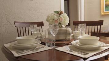 A dining table set with white plates, bowls, cutlery, and a vase of flowers.