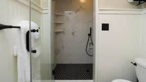 Un baño con cabina de ducha de vidrio, inodoro blanco y toallero con toallas blancas.