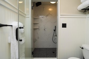 A bathroom with a glass shower enclosure, a white toilet, and a towel rack with white towels. - Historic Downtown Stay on the Square (Lebanon)