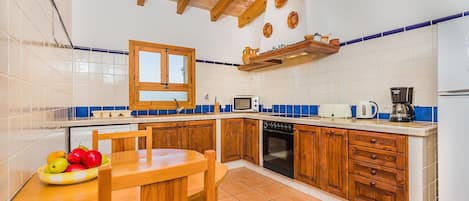 Una cocina con gabinetes de madera, salpicadero de azulejos, estufa, microondas y cafetera.