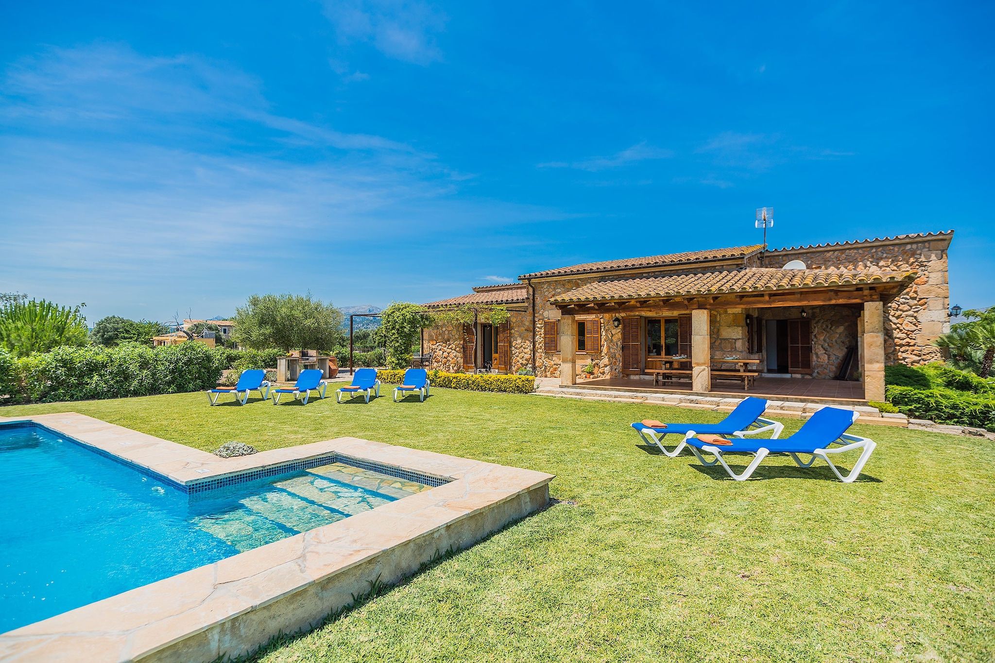 A poolside area with a stone building, outdoor seating, and a clear sky.