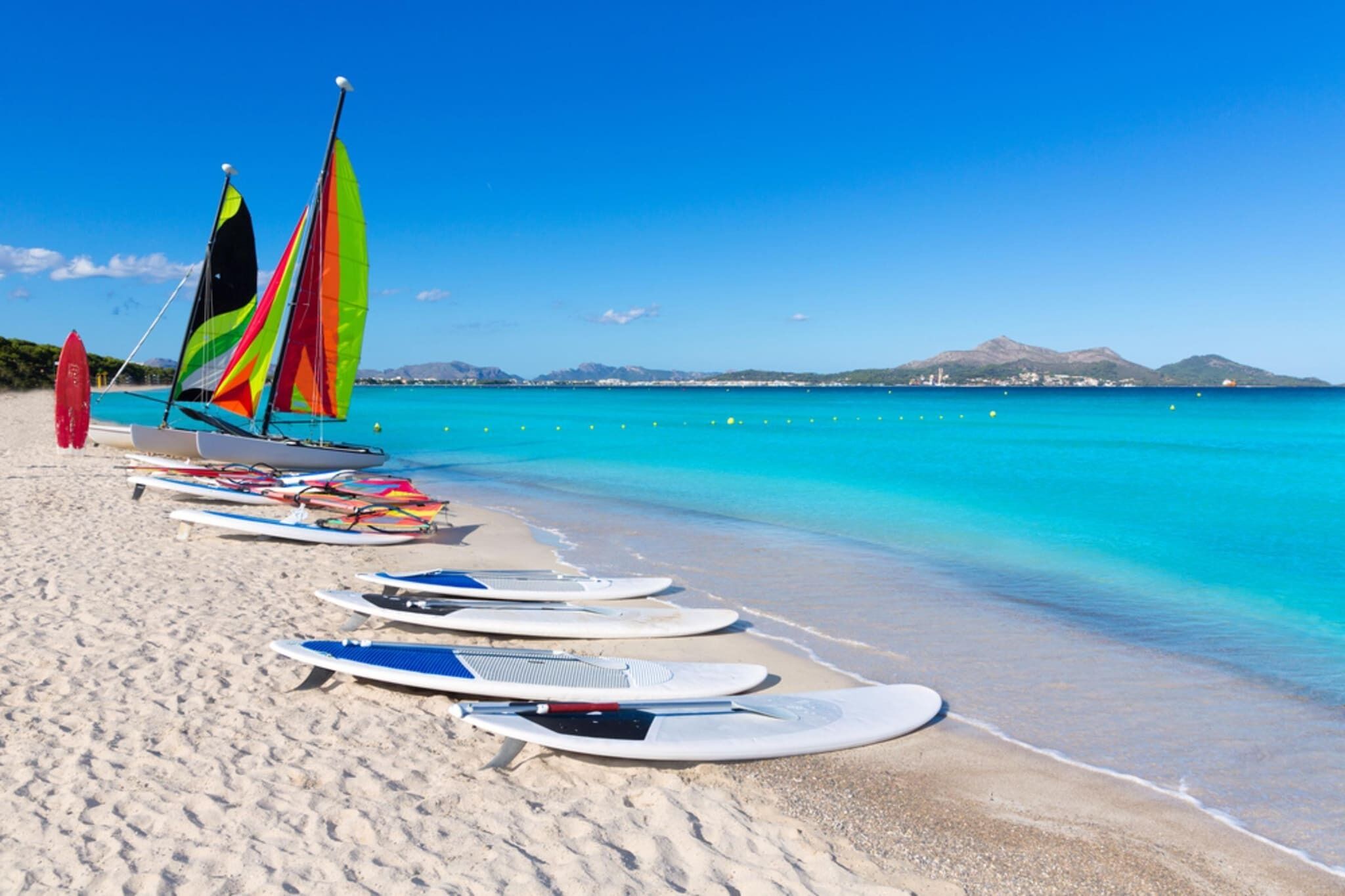 Une plage avec des planches de surf et un voilier.