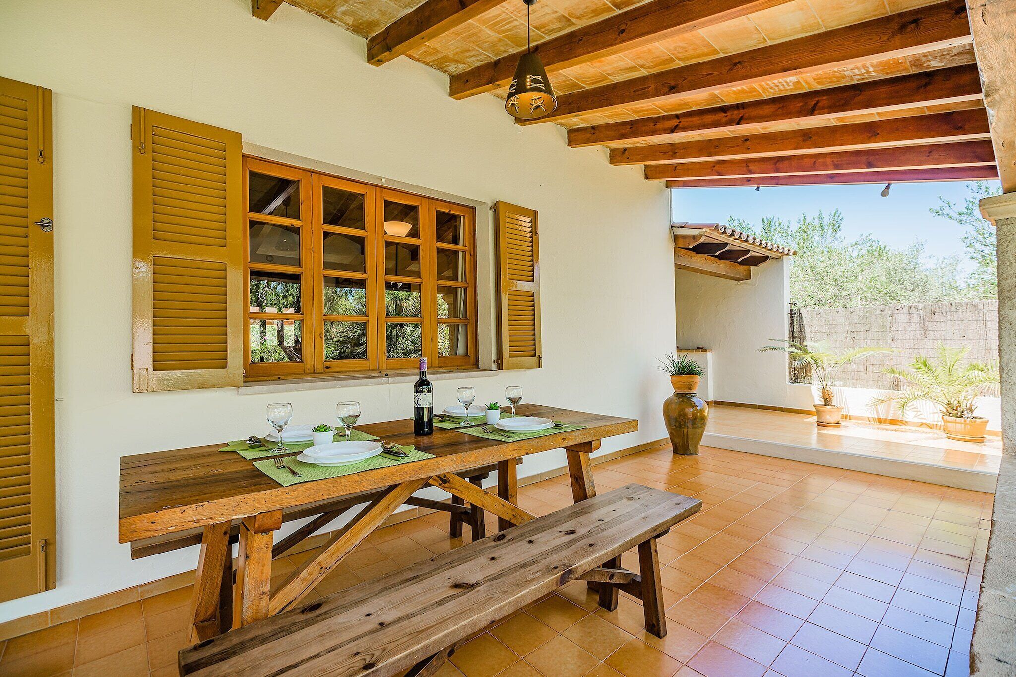 Une table à manger en bois avec un banc, une fenêtre avec des volets et une vue sur l’extérieur.