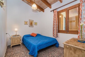 A bedroom with a bed, a nightstand, a lamp, a window with curtains, and artwork on the wall. - Rustic Country Villa with Private Pool (Pollensa / Pollença)